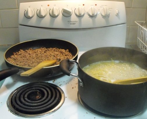 Photograph of mince meat cooking in a frying pan on a stove top and spaghetti pasta boiling in a pot